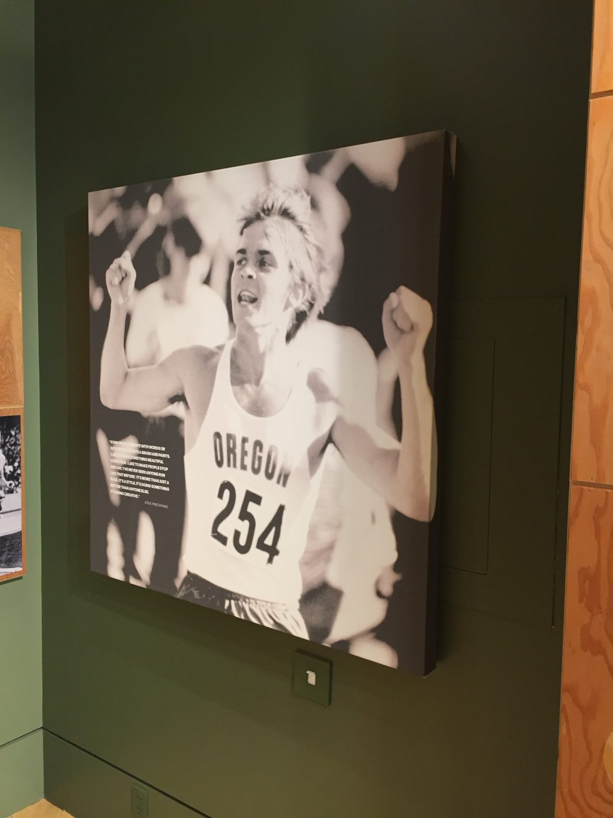 A large black-and-white canvas print at the exhibit of Pre finishing a race in his Oregon singlet, number 254, arms raised