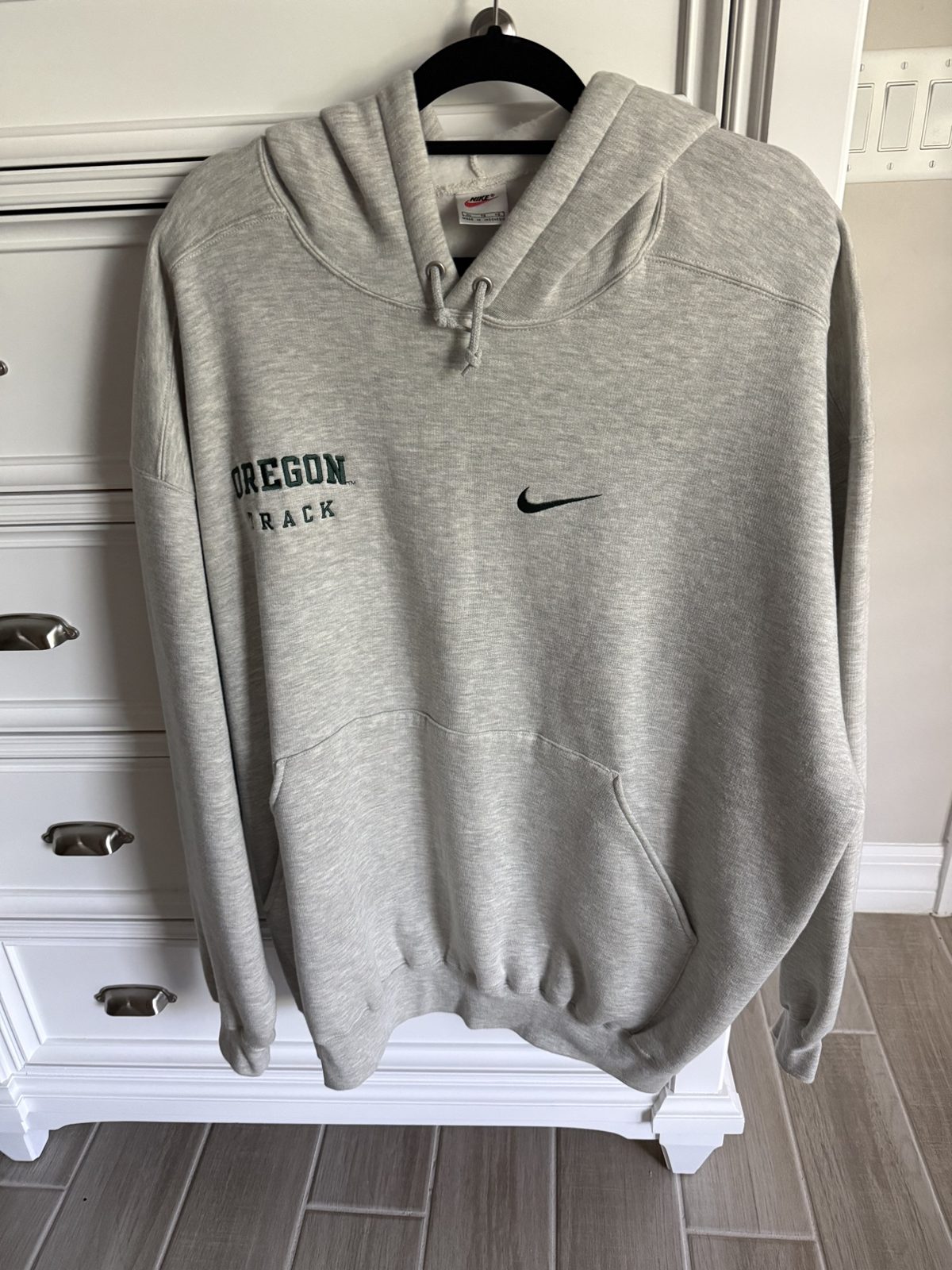 Vintage Nike Center Swoosh Oregon Track hoodie — front view: heather grey hoodie hanging up with OREGON TRACK embroidery, a center swoosh and a kangaroo pocket