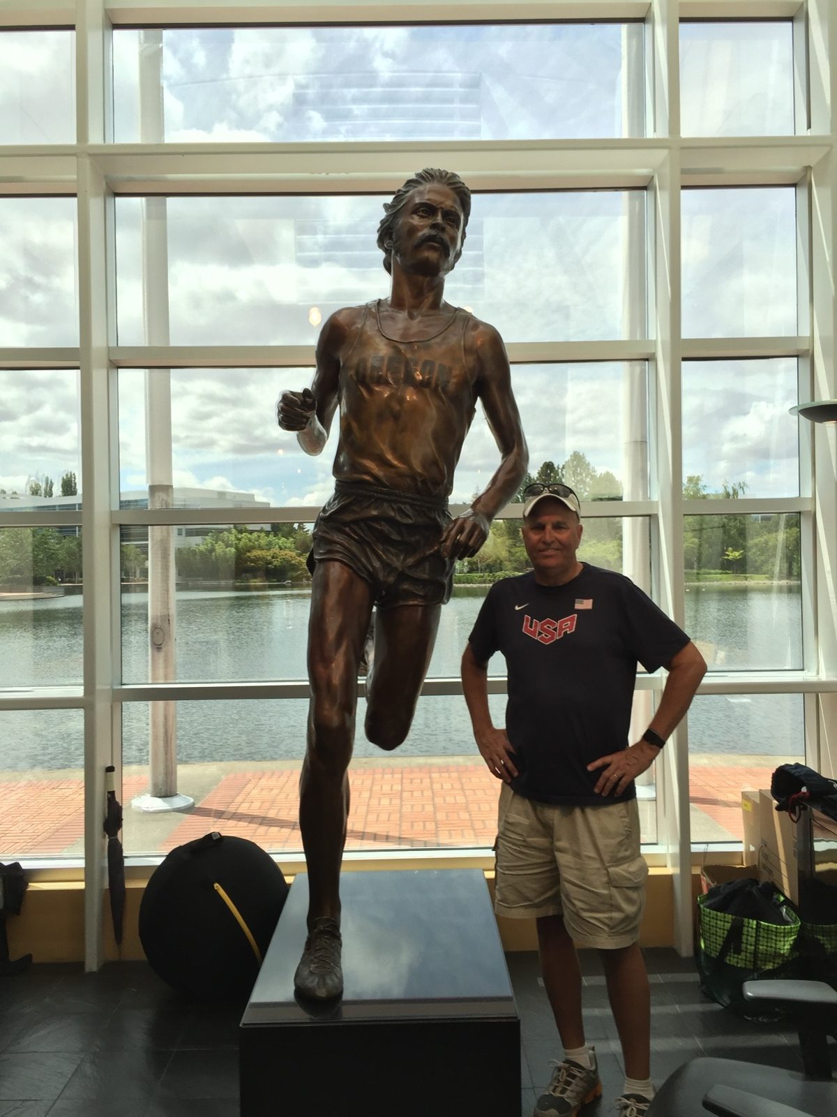 Kurt standing beside the life-size bronze statue of Steve Prefontaine in front of the windows at Nike Headquarters